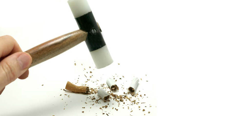 Una mano con un martillo destroza un cigarro, dejar de fumar